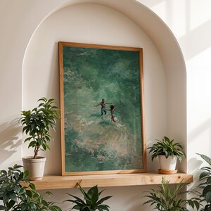 May include: A framed art print featuring an abstract painting of two figures in a green body of water. The artwork is displayed on a wooden shelf, surrounded by potted plants. The frame is made of light brown wood.