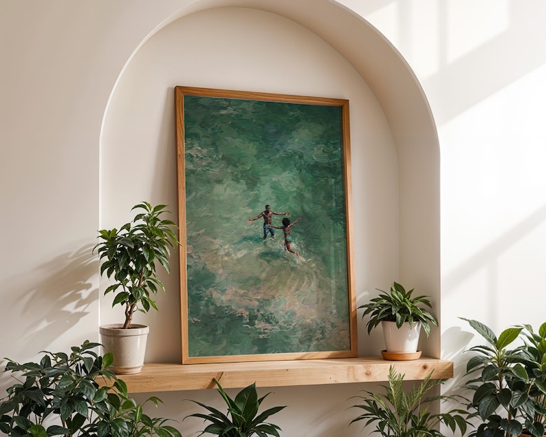 May include: A framed art print featuring an abstract painting of two figures in a green body of water. The artwork is displayed on a wooden shelf, surrounded by potted plants. The frame is made of light brown wood.