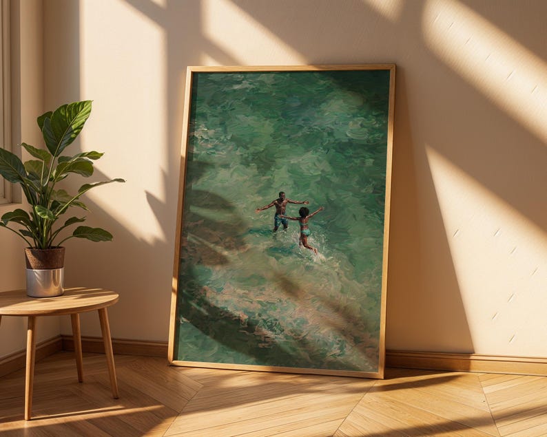 May include: A framed art print depicts two people in a turquoise ocean. The artwork has a warm, natural wood frame. The figures are in the water with their arms outstretched, creating a sense of joy and movement. The art is leaning against a wall.
