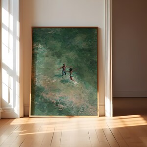 May include: A framed art print depicts two figures in a green ocean. The artwork, with a gold frame, shows the figures with their arms outstretched, creating a sense of movement. The scene is set against a backdrop of green and white water.