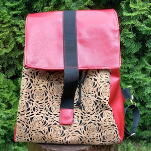 May include: Red backpack with a flap closure and black strap. The front panel features a pattern of tan roses on a black background. The bag has a black strap and gold-colored hardware.