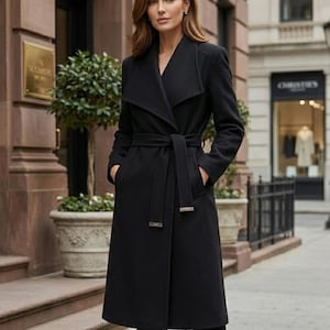 May include: A black coat with a wrap-style design and a matching belt. The coat features a wide collar and is worn over black pants. The image is taken outdoors, with a building in the background.