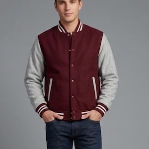 Può includere: Una giacca college bordeaux e grigia con dettagli a righe bianche sul colletto, sui polsini e sull'orlo. La giacca ha una chiusura con bottoni e due tasche anteriori. Le maniche sono grigie e il corpo è bordeaux. La persona indossa jeans blu.