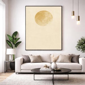 Peut inclure: Grande affiche encadrée d'art abstrait avec un cercle jaune doré sur fond crème. L'œuvre est suspendue au-dessus d'un canapé blanc avec des coussins aux tons neutres. Une table basse noire et des plantes d'intérieur complètent le décor.