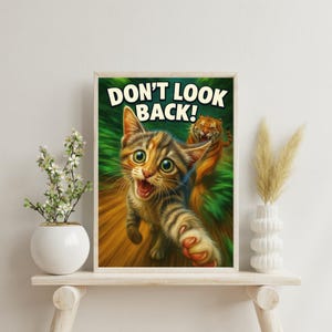 Peut inclure: Illustration encadrée d'un chat de dessin animé aux grands yeux et à la bouche ouverte, tendant une patte vers le spectateur. Le texte "DON'T LOOK BACK!" est au-dessus du chat. Un tigre est en arrière-plan.