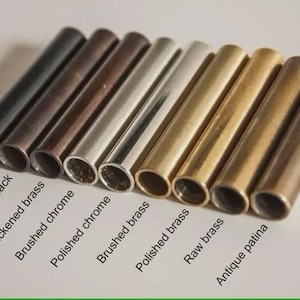 May include: A collection of cylindrical metal tubes in various finishes, including matte black, antique black, and polished chrome. The image displays a range of colors from dark to light, with labels identifying each finish. The tubes are arranged in a diagonal row.