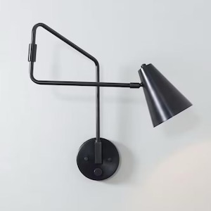 May include: A black wall-mounted light fixture with a cone-shaped shade and a swivel arm. The light fixture has a modern design and is perfect for adding a touch of style to any room.