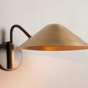 May include: A brass and black wall sconce with a curved arm and a wide, round, angled shade.