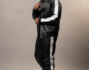 Può includere: Giacca e pantaloni in pelle nera con strisce bianche. La giacca ha una chiusura con bottoni e un colletto. I pantaloni hanno una vita con coulisse. L'outfit è completato da scarpe da ginnastica nere.