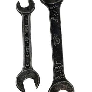 Puede incluir: Dos llaves fijas antiguas con un acabado oscuro y envejecido. La llave más pequeña está marcada con "Snail Brand" y "2". La llave más grande tiene marcas de tamaño, incluyendo "5/8 F" y "3/8 W".