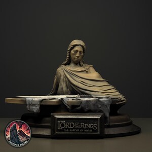 Op de afbeelding: Een gebeeldhouwde buste van een figuur met gevlochten haar en gedrapeerde kleding, geplaatst achter een plat oppervlak met een metalen zwaardfragment. Een rechthoekig plaatje op de basis toont de tekst THE LORD OF THE RINGS THE SHARDS OF NARSIL.