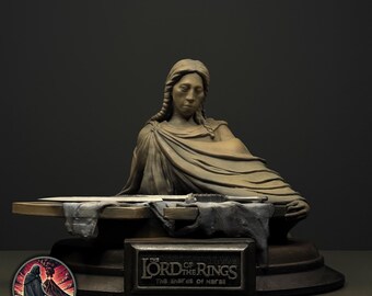 Può includere: Un busto scolpito di una figura con capelli intrecciati e abiti drappeggiati, posizionato dietro una superficie piana che sostiene un frammento di spada metallica. Una targa rettangolare sulla base mostra il testo THE LORD OF THE RINGS THE SHARDS OF NARSIL.