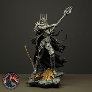 Op de afbeelding: Een gedetailleerd zilverkleurig gepantserd figuur op een rotsachtige basis, met een helm met stekels en een donkere wapperende cape. Het figuur houdt een hoge strijdhamer vast, met een goudkleurige helm en schildstuk op de grond in de buurt.