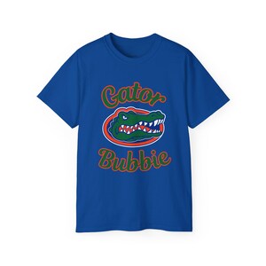 May include: Royal blue t-shirt with a graphic of a green alligator head inside a red and blue oval. The words "Gator" and "Bubbie" are in green and orange script above and below the alligator.