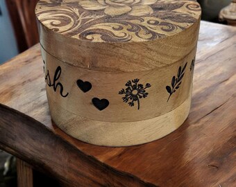May include: A wooden box with a floral design on the lid and a dandelion, two hearts, and the word "Wish" engraved on the side. The box is sitting on a wooden surface.