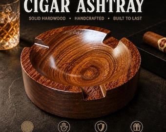 May include: A round, polished hardwood cigar ashtray with a deep, circular basin and two wide notches for resting cigars. The wood features a prominent, swirling grain pattern in rich brown tones. Text on the image reads HANDMADE HARDWOOD CIGAR ASHTRAY.