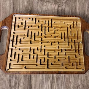 Könnte beinhalten: Holz-Labyrinth-Puzzle-Tablett mit einem komplexen Labyrinth-Design. Das Tablett hat ein hellbraunes Bambus-Labyrinth, das in einen dunkelbraunen Holzrahmen mit Griffen eingesetzt ist. Ein klassischer Denksport.