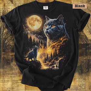 May include: A black short-sleeved t-shirt featuring a graphic print of a large cat face and a smaller cat standing on a rock. The scene includes a full moon, a dark forest, and glowing golden light effects. The word Black is printed in the corner.