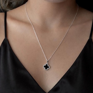 May include: A silver necklace with a black clover pendant. The clover is outlined with small, clear crystals. The necklace is displayed against a black background.