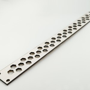 May include: A long, narrow, silver-colored metal strip featuring a repeating pattern of small hexagonal cutouts arranged in two parallel rows. The strip has two circular holes at each end, providing a functional design for mounting or attachment.