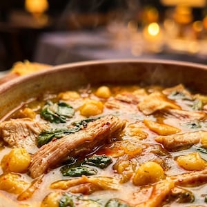 May include: A close-up shot of a hearty stew in a rustic brown bowl. The stew features chunks of meat, golden dumplings, and vibrant green spinach leaves, all simmering in a rich, flavorful broth. Steam rises from the warm dish.