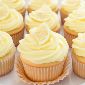 May include: A close-up of a group of lemon cupcakes with a white frosting and a lemon slice on top. The cupcakes are arranged in a circle on a white surface.