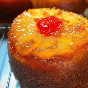 Può includere: Una torta rovesciata all'ananas di colore marrone dorato con una ciliegia rossa in cima. La torta è glassata e ha una finitura lucida.