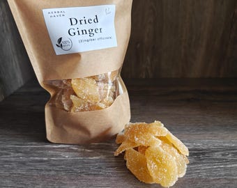 May include: A brown paper bag with a clear window filled with dried ginger slices. The bag has a label that reads "Dried Ginger" and "Herbal Haven". A small pile of ginger slices sits in front of the bag on a wooden surface.