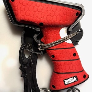May include: A red and black plastic gun-shaped device with a textured grip and the word "BUBBA" printed on the side. The device has a black clip and a black strap attached to it.