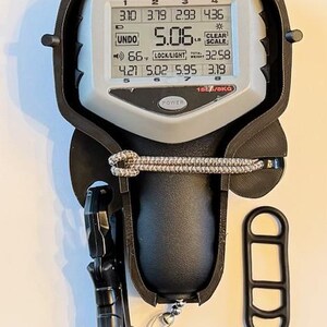 May include: A digital fishing scale with a black and gray case, displaying weight in pounds. The screen shows multiple weight readings and a total weight of 32.58. Includes a handle and a separate black accessory.