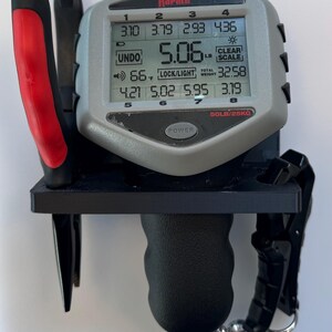 May include: A gray Rapala digital fish scale with a black handle and a black hook. The scale displays a weight of 5.06 pounds, a total weight of 32.58 pounds, and a temperature of 66 degrees Fahrenheit. The scale also has a clear scale button, a lock/light button, and a power button.