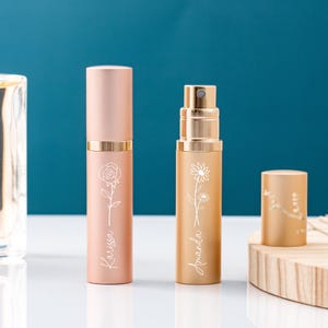 Pode incluir: Dois atomizadores de perfume, um em ouro rosa e outro em ouro, com desenhos florais e nomes. O atomizador em ouro rosa tem um desenho de rosa e o nome "Karissa". O atomizador dourado tem um desenho de margarida e o nome "Amanda".