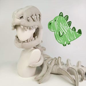 May include: A plush dinosaur costume in light gray, featuring a detailed skull headpiece and spine. A green crayon drawing of a dinosaur is on the right. The costume is designed to fit over the head and shoulders.