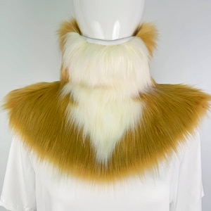 May include: A faux fur collar in shades of tan and cream. The collar is designed to be worn around the neck and shoulders. The fur is long and fluffy, creating a soft and luxurious look. The collar is likely for cosplay or costume use.