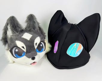 May include: Two plush animal heads: a gray and white wolf head with blue eyes and a black cat head with iridescent accents. The wolf head has a pink tongue sticking out. The cat head has large, pointed ears.