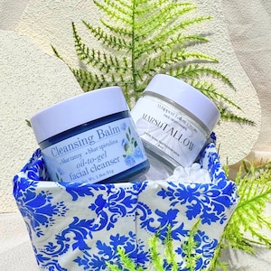 May include: Two skincare products in a blue and white patterned basket. One jar is labeled "Cleansing Balm" and the other "Whipped Tallow Cream". The cleansing balm is blue and the cream is white. The basket is decorated with blue floral designs.