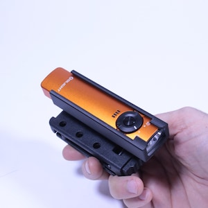 May include: An orange and black flashlight with the brand name "OLIGHT" printed on the top. The flashlight has a black clip attached to the bottom. The flashlight has a black button and four small indicator lights.