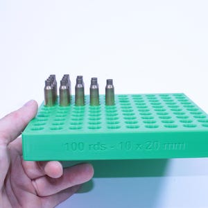 Peut inclure: Un support vert pour munitions contenant plusieurs cartouches en laiton. Le support est étiqueté "100 rds - 10 x 20 mm". Il est conçu pour contenir 100 cartouches. Fabriqué en plastique.