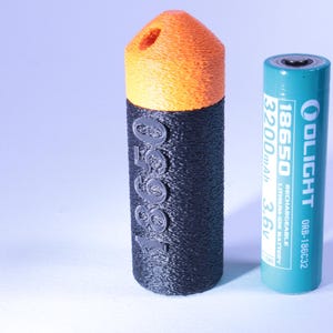 Op de afbeelding: Een zwart-oranje 3D-geprinte batterijhouder naast een turquoise 18650 oplaadbare lithium-ion batterij. De houder is cilindrisch met de cijfers "18650" erop. De batterij heeft de merknaam "OLIGHT".