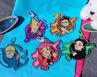 May include: Five acrylic keychains featuring illustrated characters in various poses, each set against a distinct colored gear-shaped background in purple, orange, blue, pink, and green, with matching plastic clasps attached to the top of each piece.