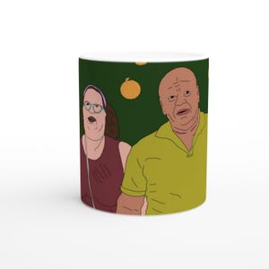 May include: A white ceramic mug with a green background featuring a cartoon illustration of two people. The people are wearing casual clothing and are looking up. There are orange pumpkins scattered on the background.