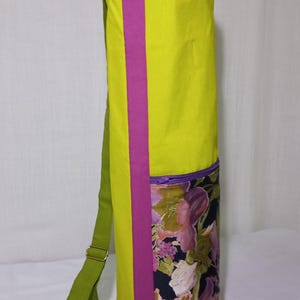 Könnte beinhalten: Eine limettengrüne Yogamatten-Tasche mit einem vertikalen magentafarbenen Streifen auf der Vorderseite. Die Tasche hat eine Tasche mit Blumendruck mit einem lila Reißverschluss und einen grünen Schultergurt. Die Tasche ist für eine Yogamatte konzipiert.