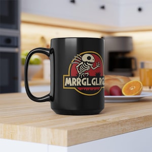 May include: Black ceramic mug featuring a cartoon skeleton design within a red and yellow circle, with the text "MRRGLGLRG". The mug has a large handle and is likely used for beverages. The design is reminiscent of a popular movie logo.