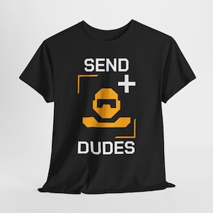Può includere: T-shirt nero con la scritta bianca "SEND + DUDES". Il design include una figura arancione stilizzata e un segno più. La maglietta è realizzata in materiale morbido.