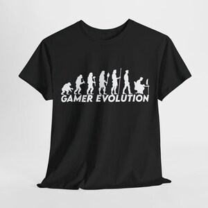 May include: Black t-shirt featuring a white graphic of the evolution of a gamer, from ape to person at a computer. The text "GAMER EVOLUTION" is below the graphic. The shirt is made of a soft material.
