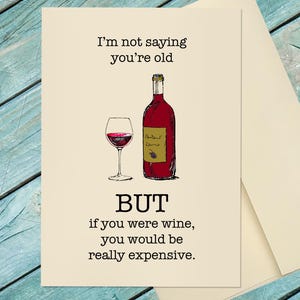 May include: Greeting card with a wine theme. The card features a red wine bottle and a glass of wine. Text on the card reads: "I'm not saying you're old, BUT if you were wine, you would be really expensive."
