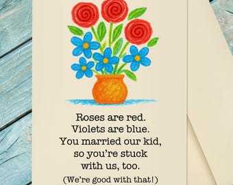 May include: A greeting card featuring a drawing of red roses and blue flowers in an orange vase. The text reads: Roses are red. Violets are blue. You married our kid, so you're stuck with us, too. (We're good with that!) The card is cream-colored.
