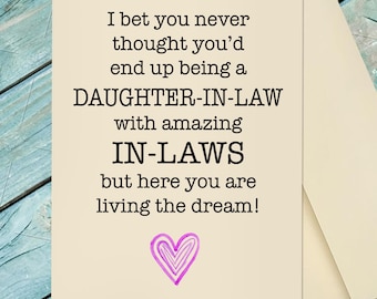 May include: A cream-colored greeting card with black text that reads: I bet you never thought you’d end up being a DAUGHTER-IN-LAW with amazing IN-LAWS but here you are living the dream! Below the text is a hand-drawn purple heart illustration.