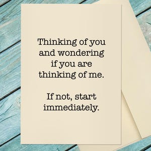May include: A rectangular cream-colored greeting card with black text that reads: Thinking of you and wondering if you are thinking of me. If not, start immediately. The card is positioned next to a matching cream-colored envelope.