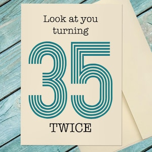 Op de afbeelding: Een cr&egrave;mekleurige verjaardagskaart met de tekst "Look at you turning 35 TWICE" in zwart en blauwgroen. Het getal 35 is gestileerd met blauwgroene concentrische lijnen. Een envelop is gedeeltelijk zichtbaar.